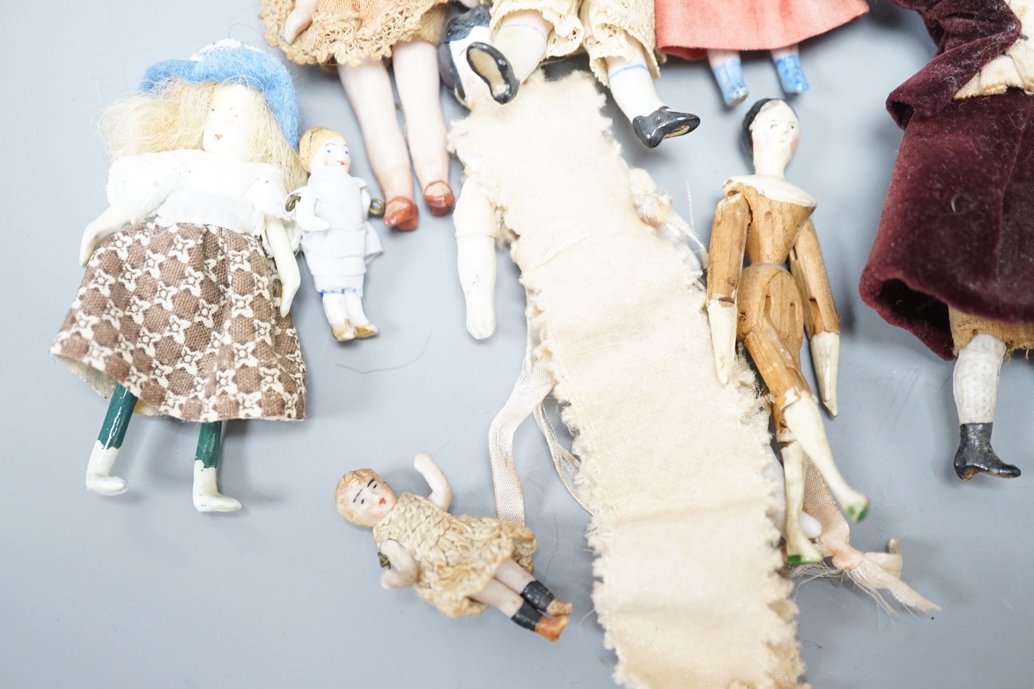 A collection of miniature bisque dolls and another larger doll in a wooden cradle, 11 dolls in total., Cradle 23.5 cms long.